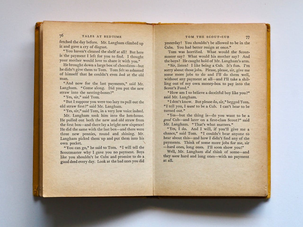 Vintage book opened to pages 76-77, displaying classic literature text in soft lighting.